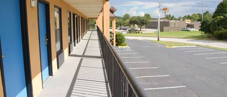 A hotel corridor with blue doors, a covered walkway, and a parking lot in the background.