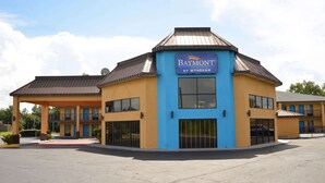 Een Baymont by Wyndham hotel met een blauw-geel gevel, een overdekte parkeerplaats en een grote parkeerplaats.