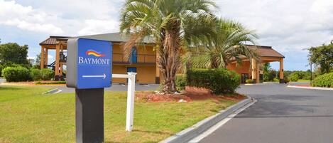 A Baymont hotel entrance with a sign, palm trees, and a parking lot.