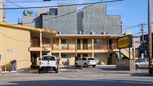 Un hôtel à la structure à deux étages, doté d’un balcon bien visible au deuxième étage et d’un parking où sont stationnées plusieurs voitures.