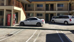 Un parking où sont garées deux voitures blanches devant un bâtiment où se trouve un distributeur automatique de Coca-Cola.
