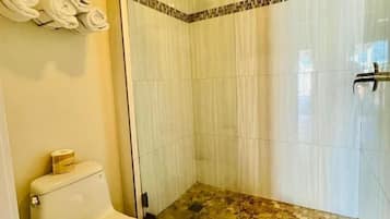 Kylpyhuone, jossa on wc, lasiseinällinen suihku ja laatoitettu lattia.