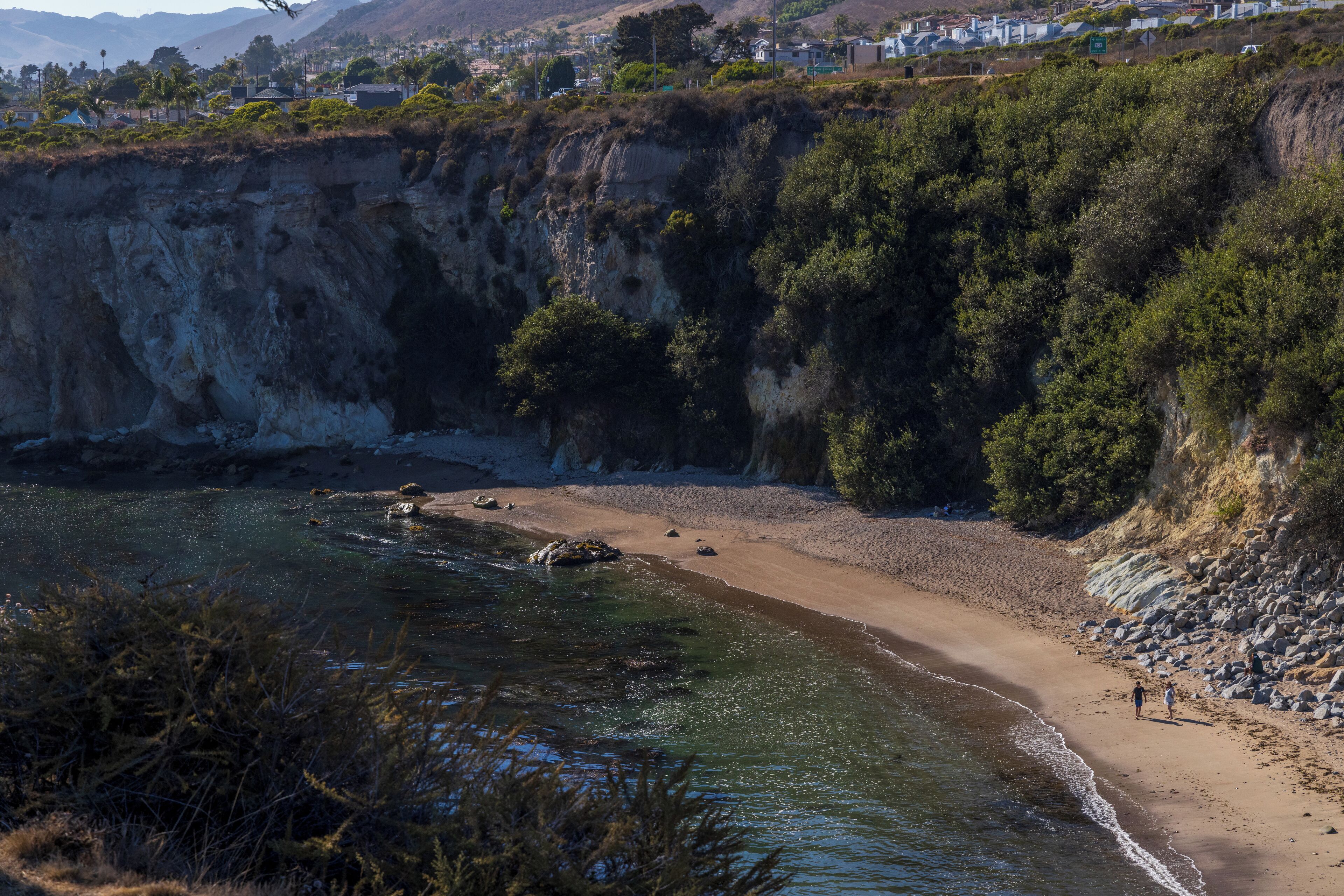 A coastal landscape with a sandy beach, rocky cliffs, and a clear view of the ocean.