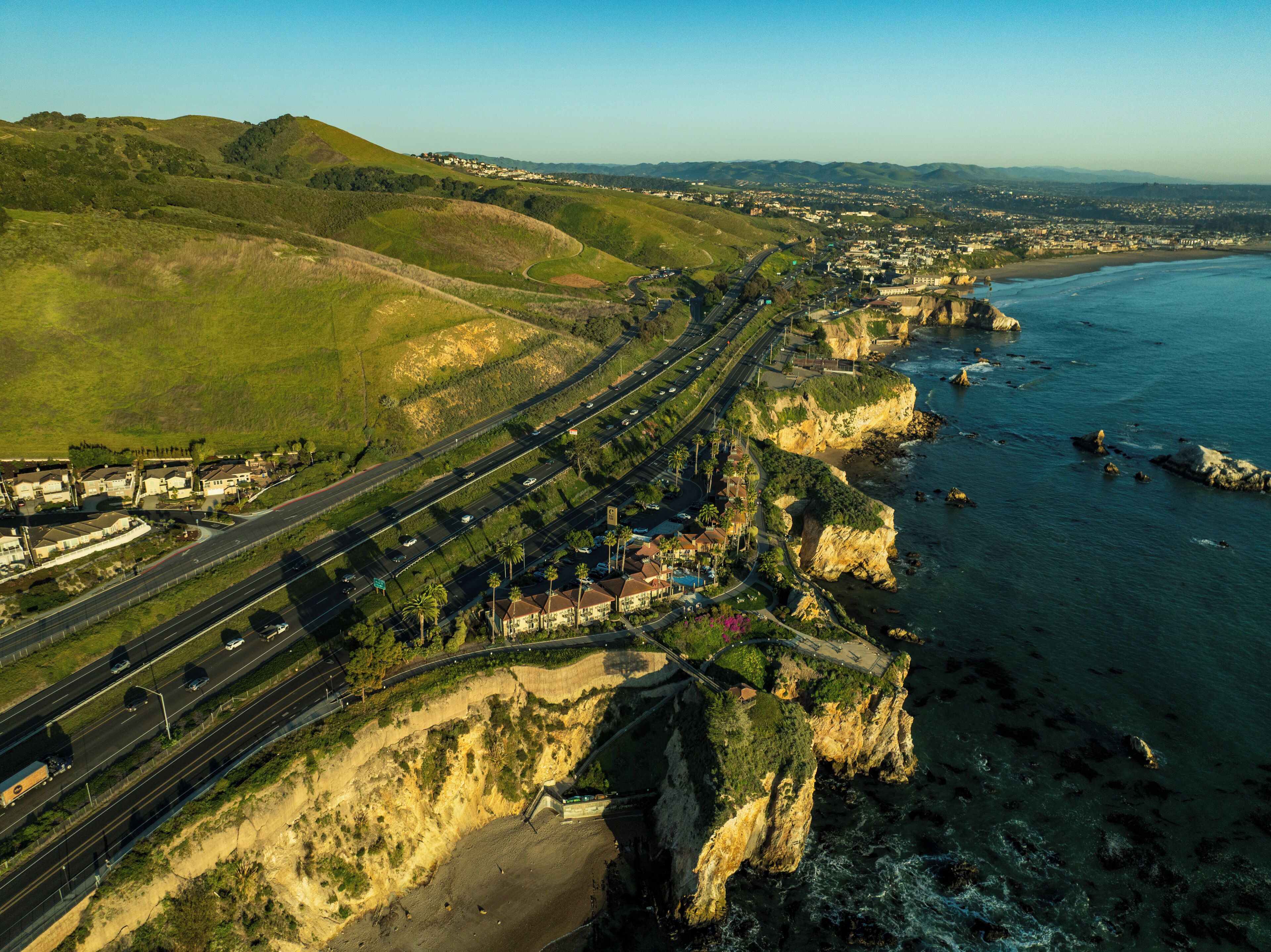 An aerial view of a coastal highway with multiple lanes, a bridge, and a beach.