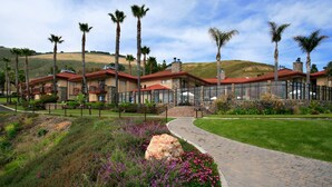 Un hotel con varios balcones, un jardín ajardinado y un paisaje montañoso al fondo.