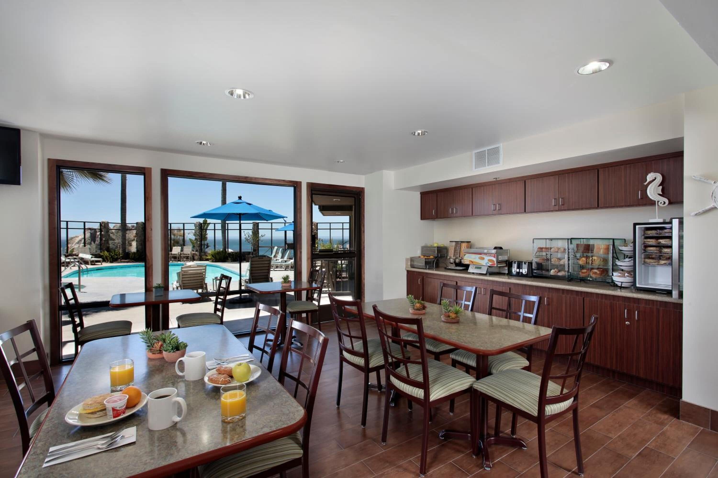 Un comedor con vista a la piscina, armarios de madera y una mesa para desayunar.