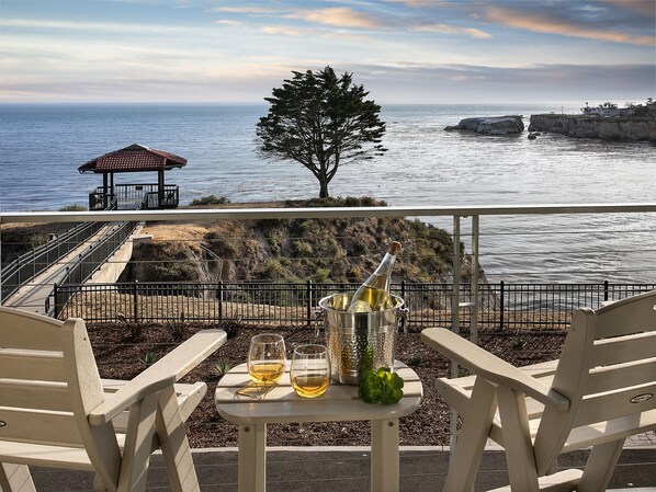 A terrace with two chairs, a table with two glasses of wine, a bottle of champagne, and a view of the ocean and rocky coastline. - Inn at the Cove (Pismo Beach)