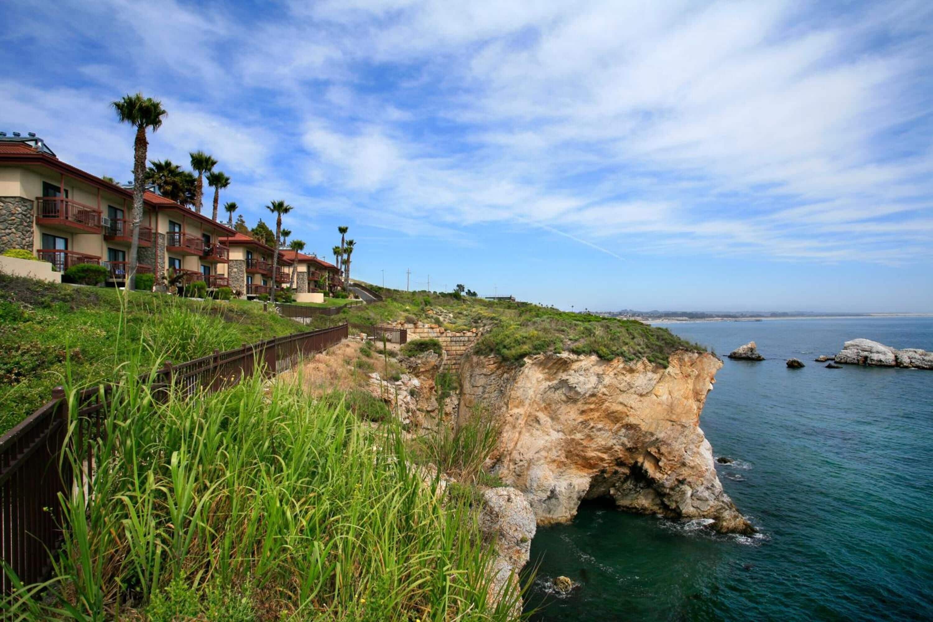 A coastal hotel with multiple balconies, a rocky cliffside, and a view of the sea.