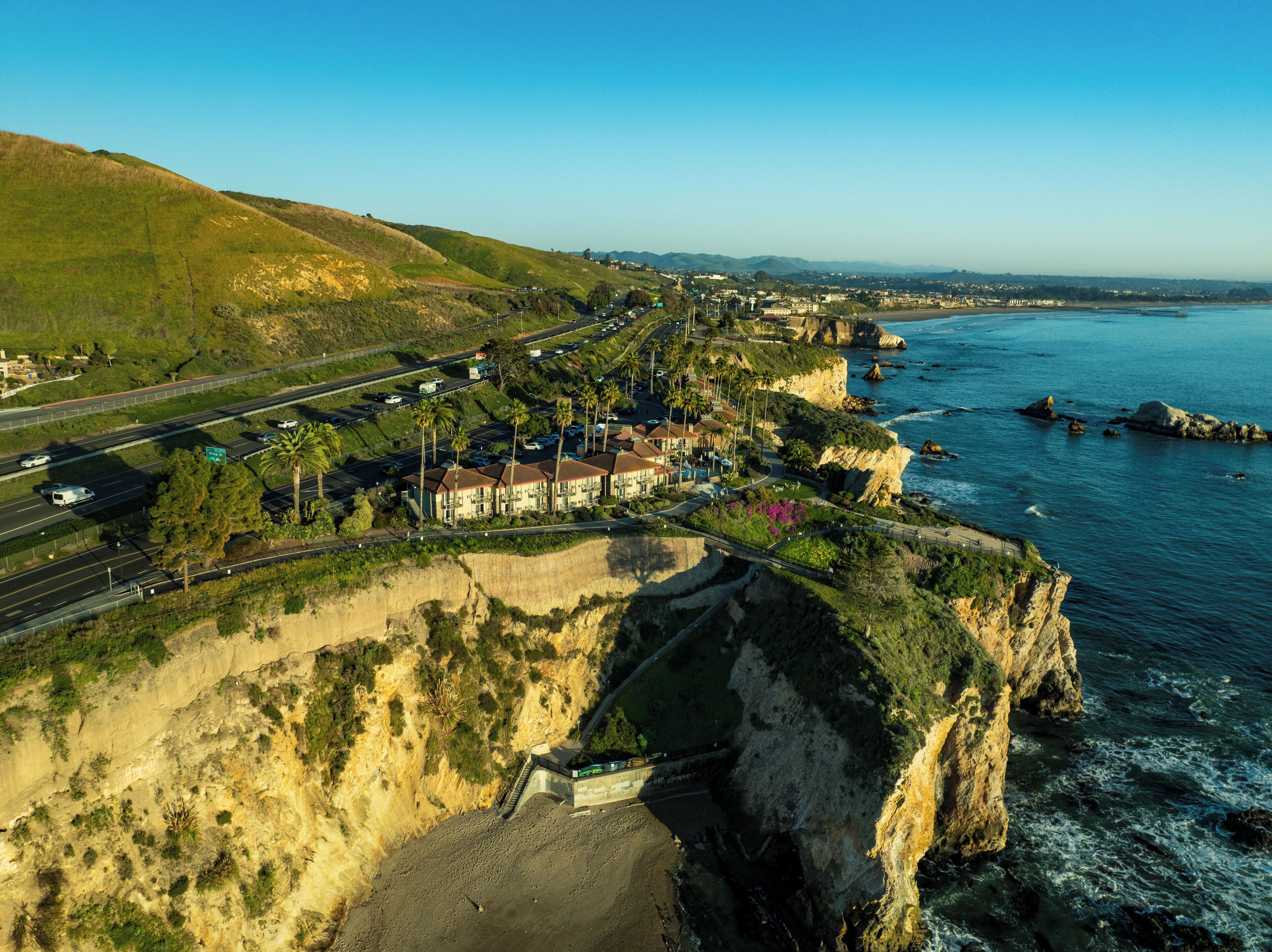 An aerial view of a coastal town with a prominent cliff, a highway, and a beach.