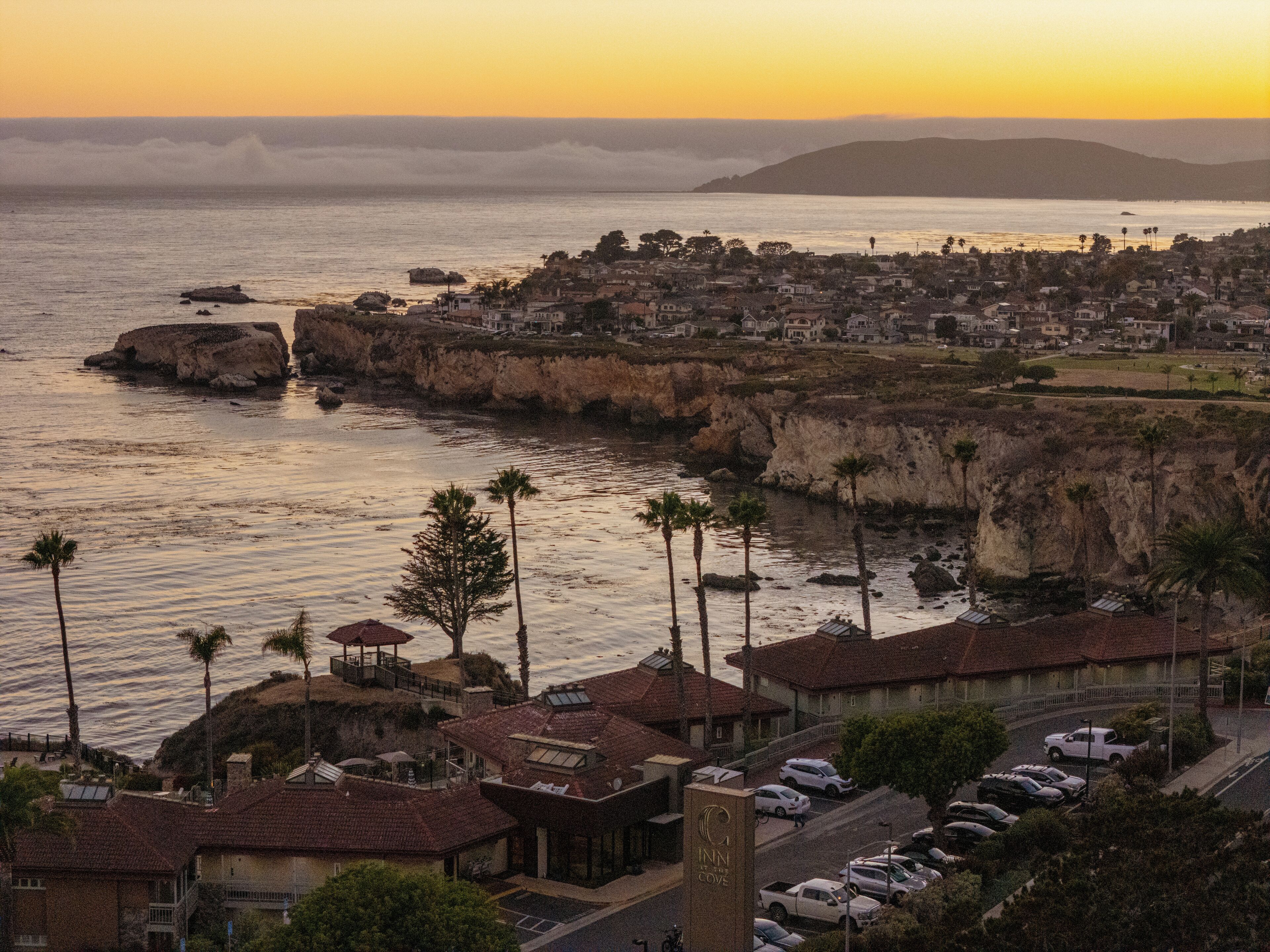 Un pueblo costero con un acantilado destacado, un puerto deportivo y un hotel con vistas al mar.
