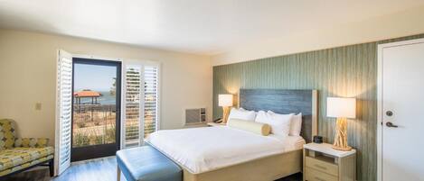 Une chambre d’hôtel avec un lit, des tables de chevet, un banc et une vue sur la plage depuis la porte.