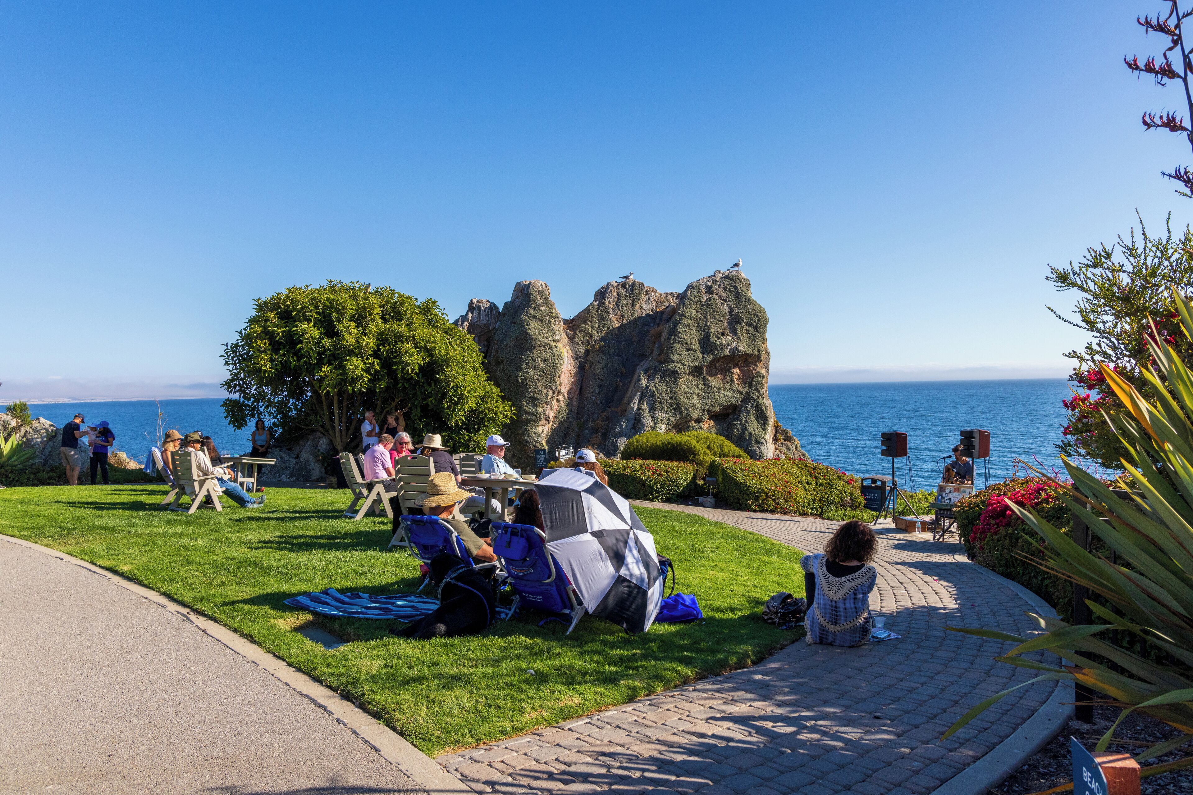 A coastal park with grassy areas, seating, and a stage for performances.