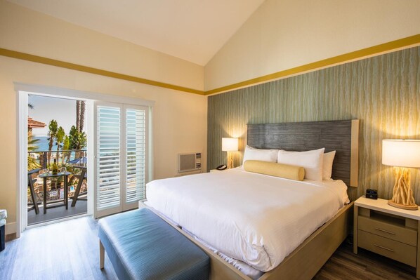 Una habitación de hotel con una cama grande, un banco, una mesita de noche y vistas al balcón exterior.