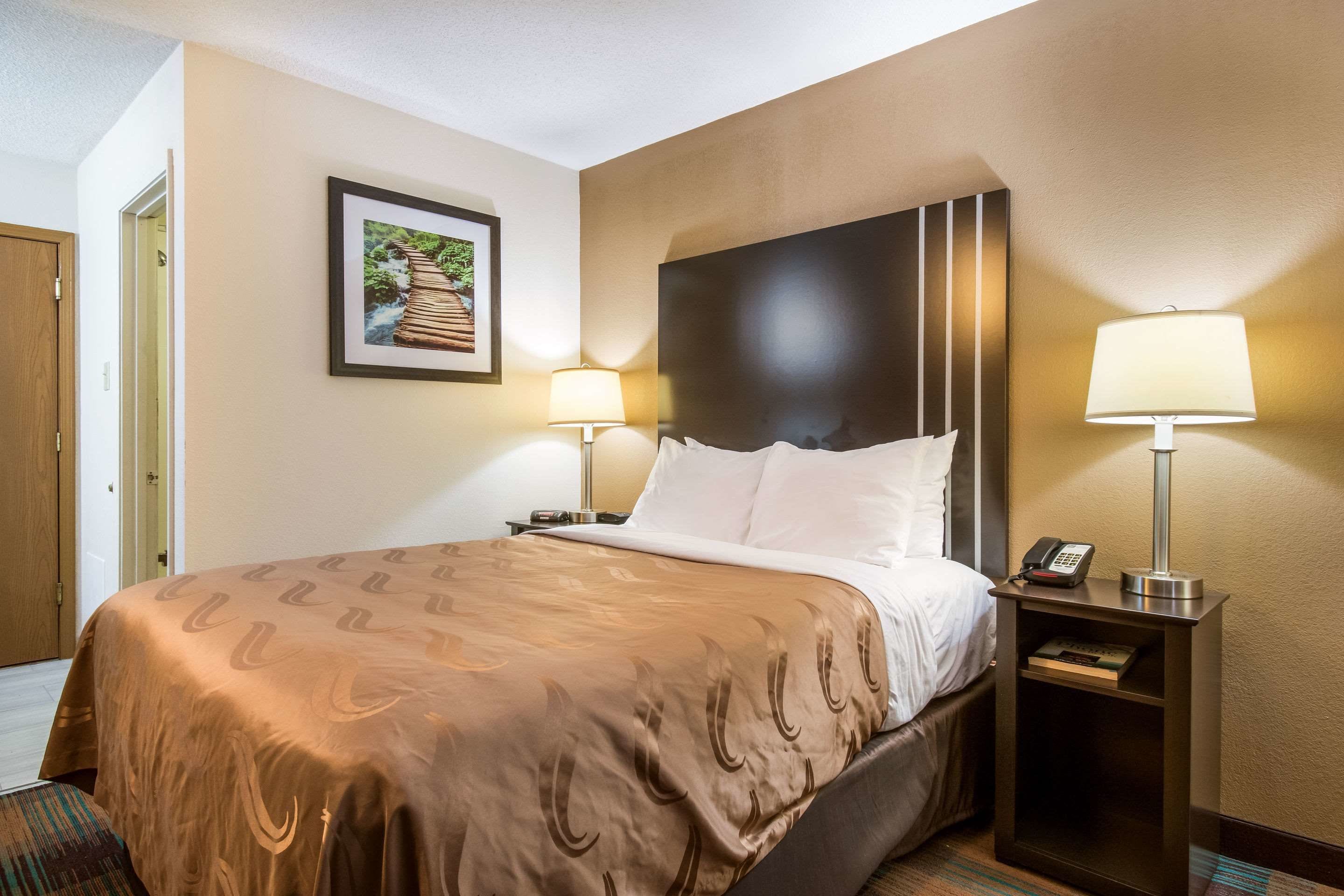 A hotel room with a large bed, two bedside lamps, a nightstand with a phone, and a framed picture on the wall.