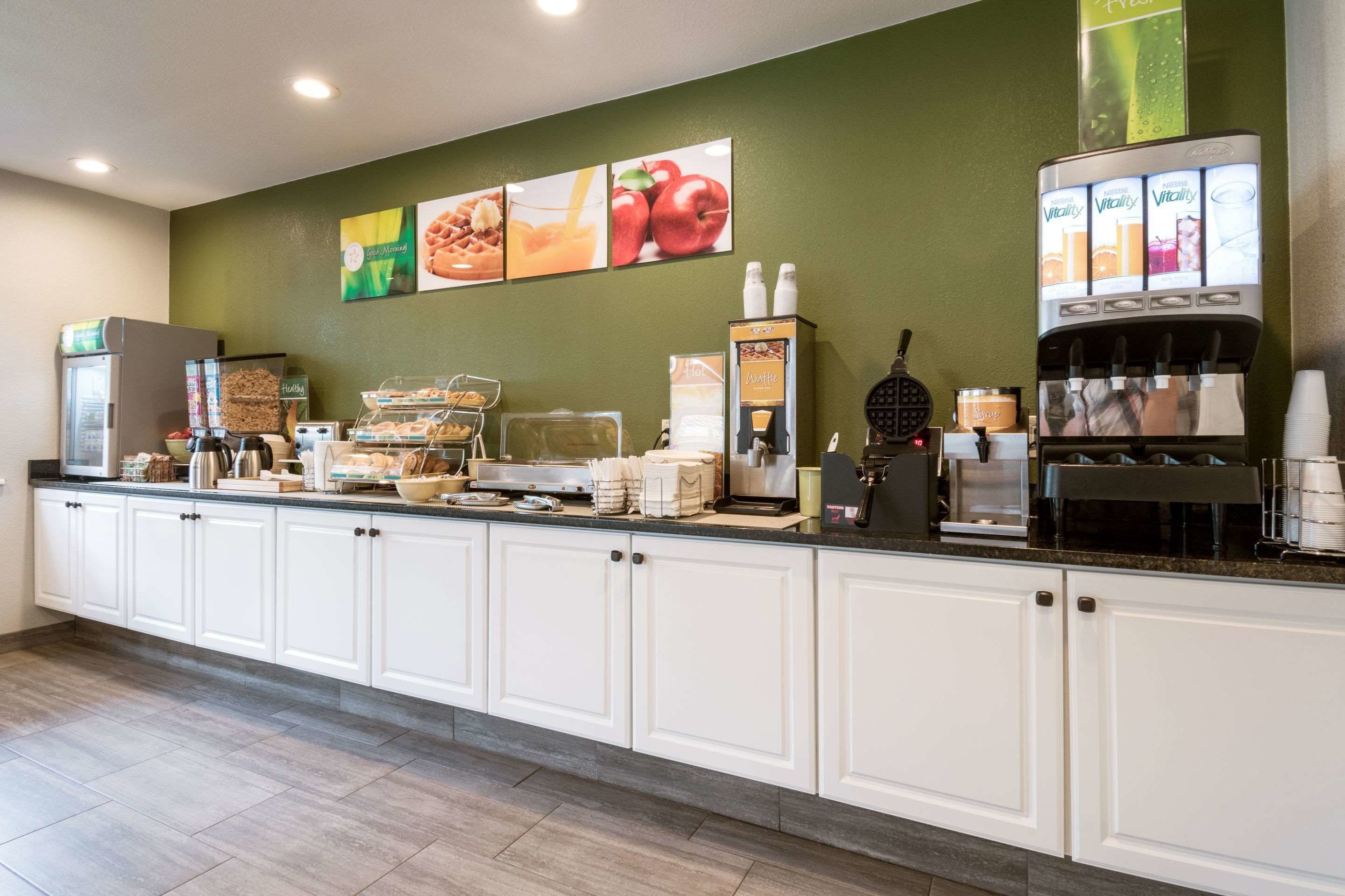 A hotel breakfast area with a self-serve coffee machine, a waffle maker, and various food items.
