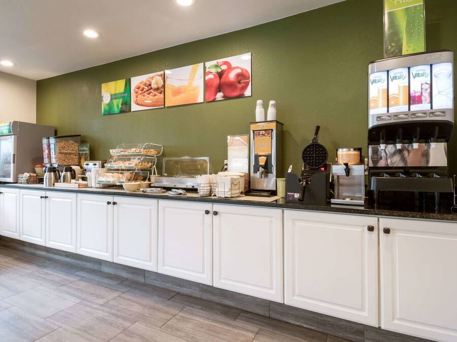 A hotel breakfast area with a self-serve coffee machine, a waffle maker, and various food items.