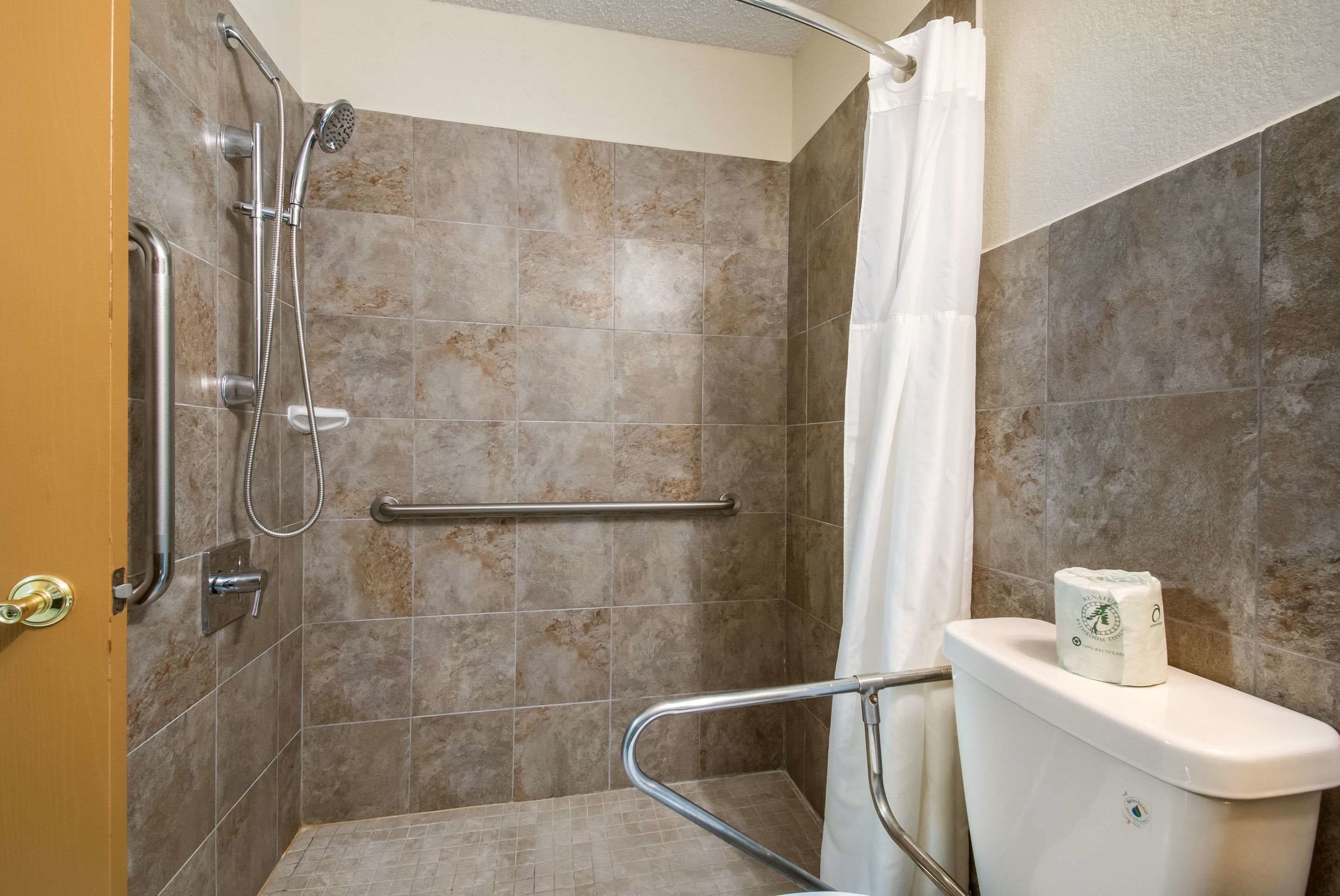 A shower area with a grab bar, a towel rack, and a toilet with a paper towel dispenser.