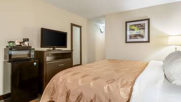 A hotel room with a bed, a TV, a microwave, a refrigerator, a desk, and a framed picture on the wall.