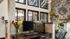 A desk with a computer, a vase of flowers, and a stone wall with a clock. - Quality Inn Bloomsburg (Bloomsburg)