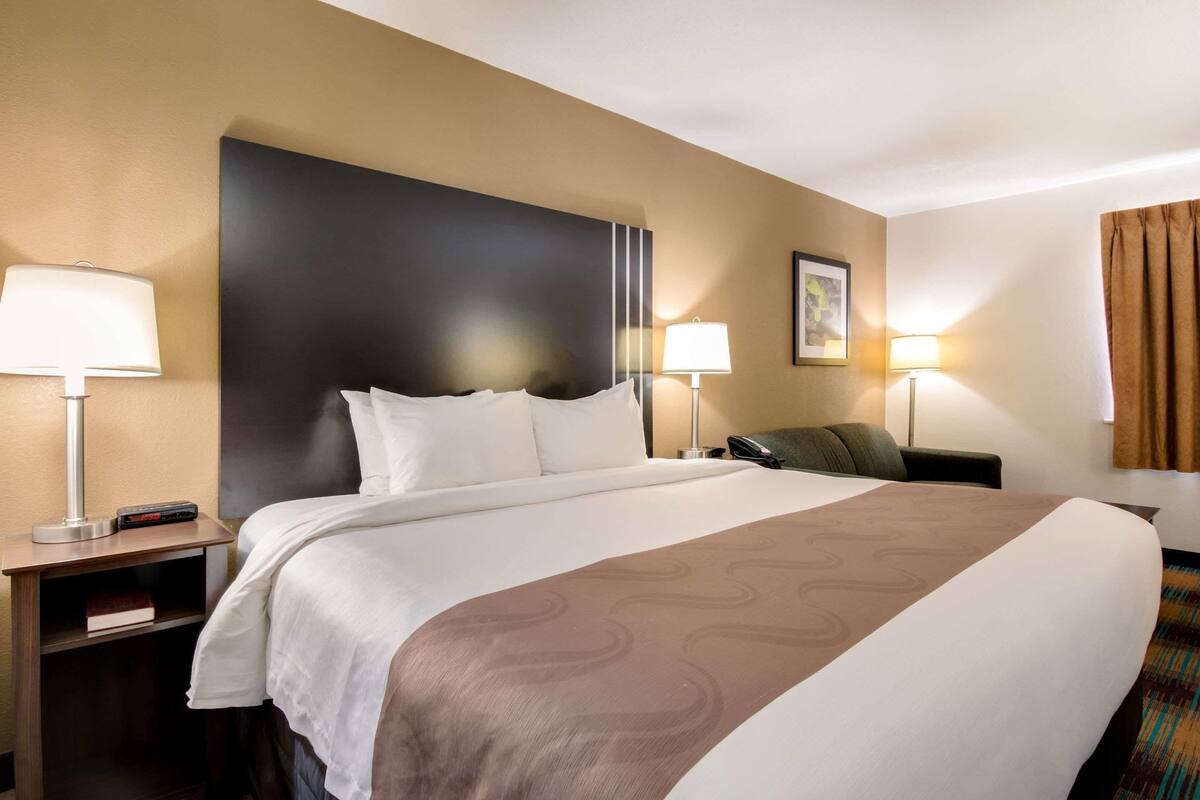 A hotel room with a large bed, two bedside tables with lamps, a chair, and a framed picture on the wall.