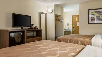 A hotel room with two beds, a TV, a mini-fridge, a microwave, and a bathroom visible through an open door.