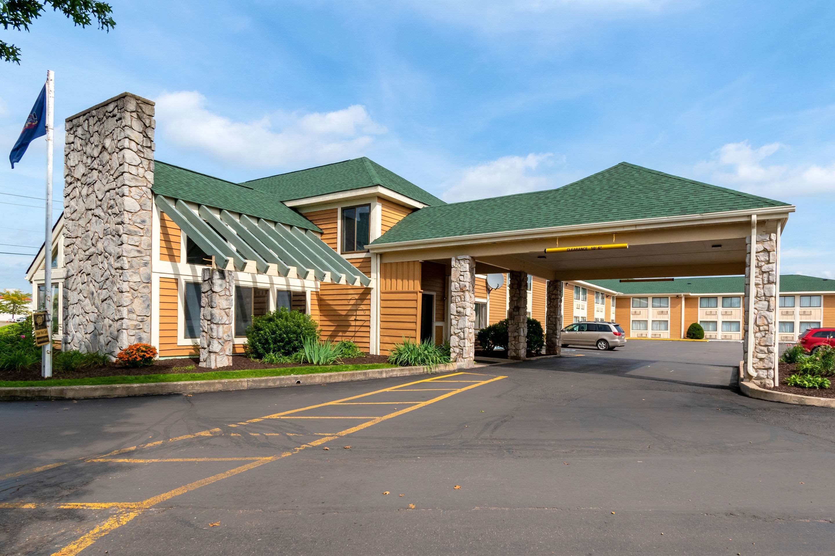A hotel with a stone facade, green roof, and a covered parking area.
