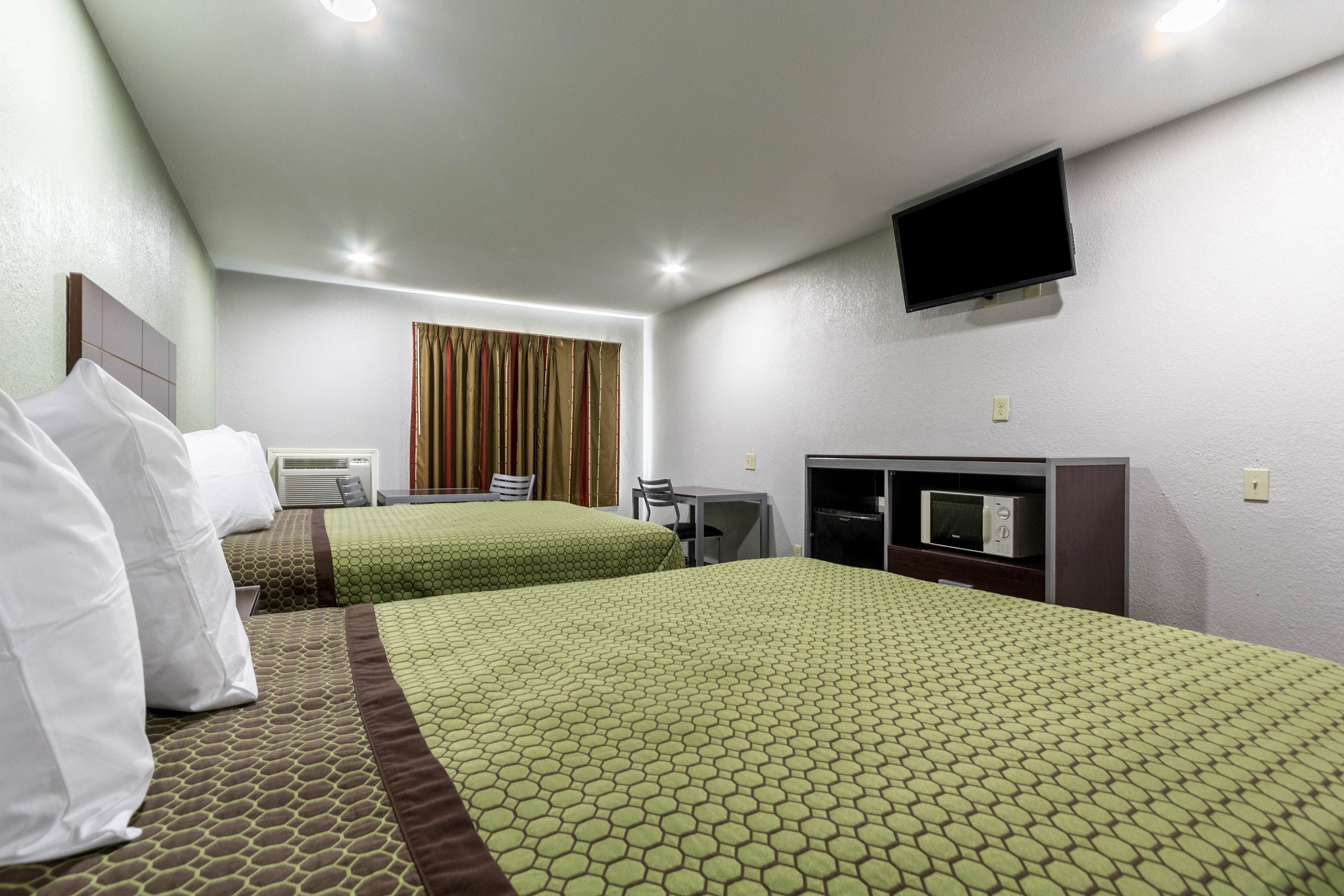 Habitación de hotel con dos camas, televisor, escritorio y microondas.