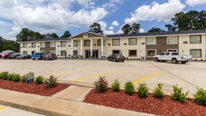 A motel with a parking lot, multiple vehicles, and a clear sky. - Scottish Inn and Suites (Tomball)