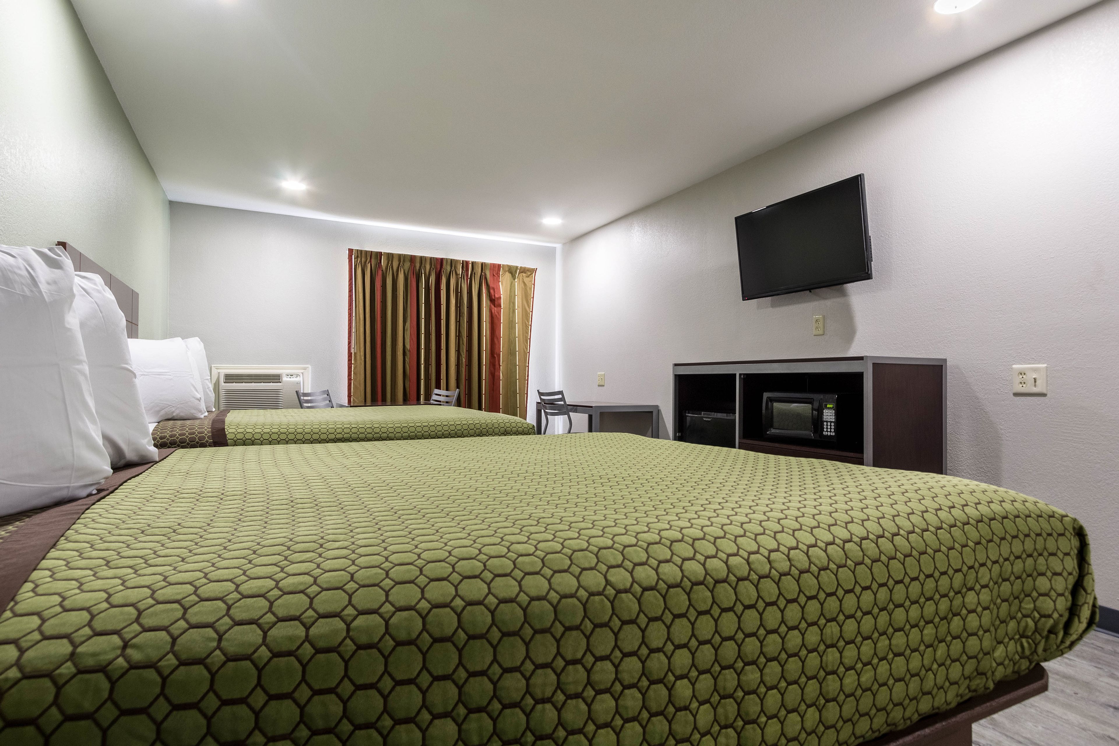 A hotel room with two beds, a television, a microwave, and a small table.