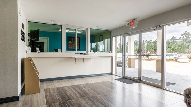 A reception area with a counter, a clock, and a view of the parking lot. - Scottish Inn and Suites (Tomball)