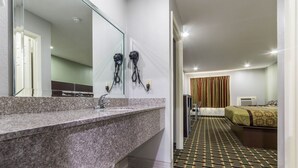 A hotel bathroom with a granite countertop, a sink, and two hair dryers mounted on the wall. - Scottish Inn and Suites (Tomball)
