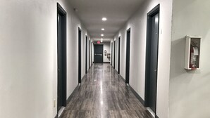 A long, narrow hallway with dark tiled flooring and white walls. - Scottish Inn and Suites (Tomball)