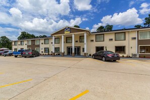 A motel with a central entrance, multiple parking spaces, and a clear sky. - Scottish Inn and Suites (Tomball)