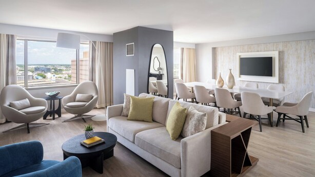 A modern living room with a sofa, armchairs, a coffee table, and a dining area with chairs and a TV.
