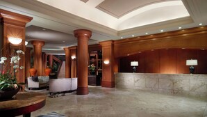 A lobby with marble flooring, wooden columns, a reception desk, and a staircase.
