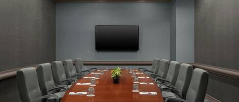 Un salón de conferencias con una larga mesa, varias sillas, un televisor de pantalla plana y un centro de mesa con planta.