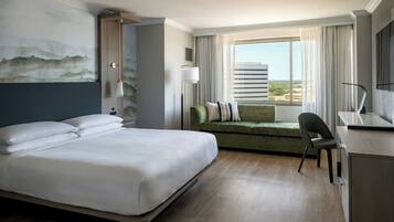 A hotel room with a large bed, a green sofa, a desk, and a view of the city through the window.