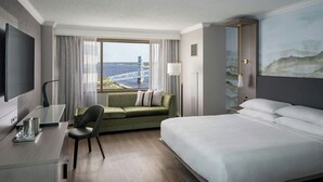 A hotel room with a large bed, a desk with a chair, a sofa, and a TV.
