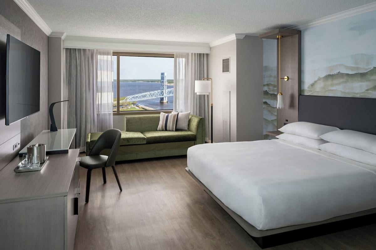 A hotel room with a large bed, a desk with a chair, a sofa, and a TV.