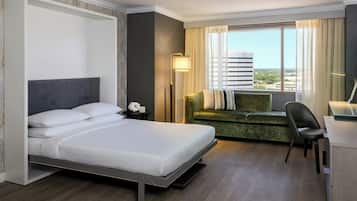 A modern hotel room with a bed, a green sofa, a desk, and a view of the city.