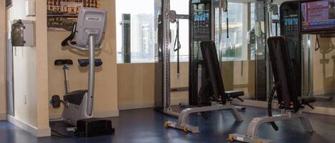 A gym with exercise equipment, a water dispenser, and a large window with a city view.