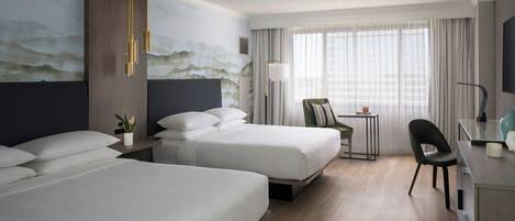 A hotel room with two beds, a desk, a chair, a lamp, and a painting on the wall.