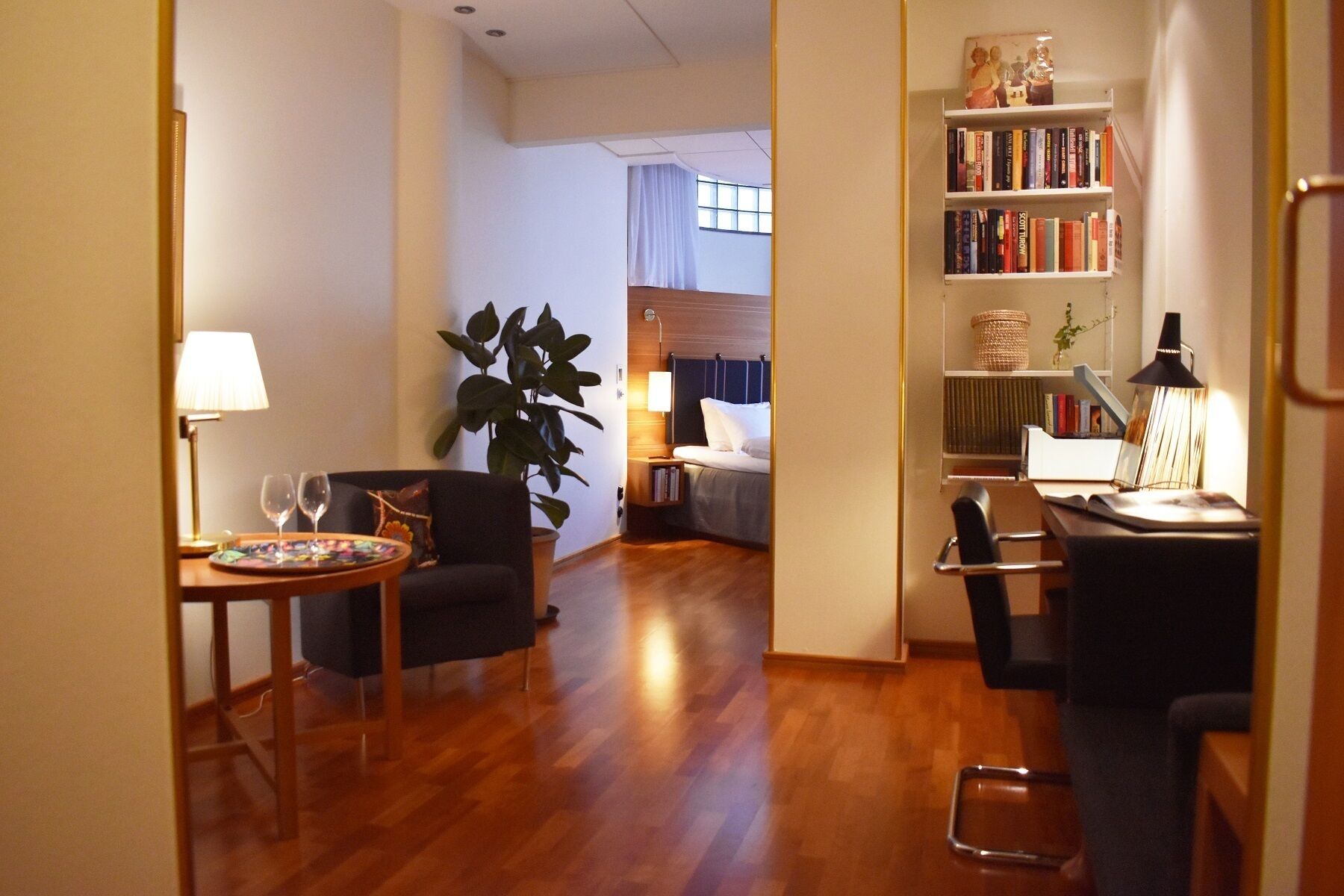 A modern living room with a sofa, a small table with a lamp, a bookshelf, and a large plant.