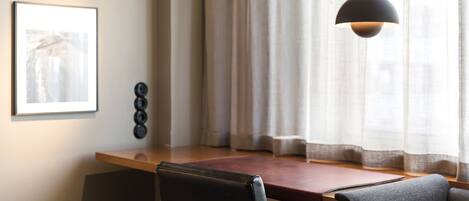 Un comedor moderno con una mesa de madera, dos sillas, una lámpara colgante, un cuadro enmarcado y una ventana con cortinas.
