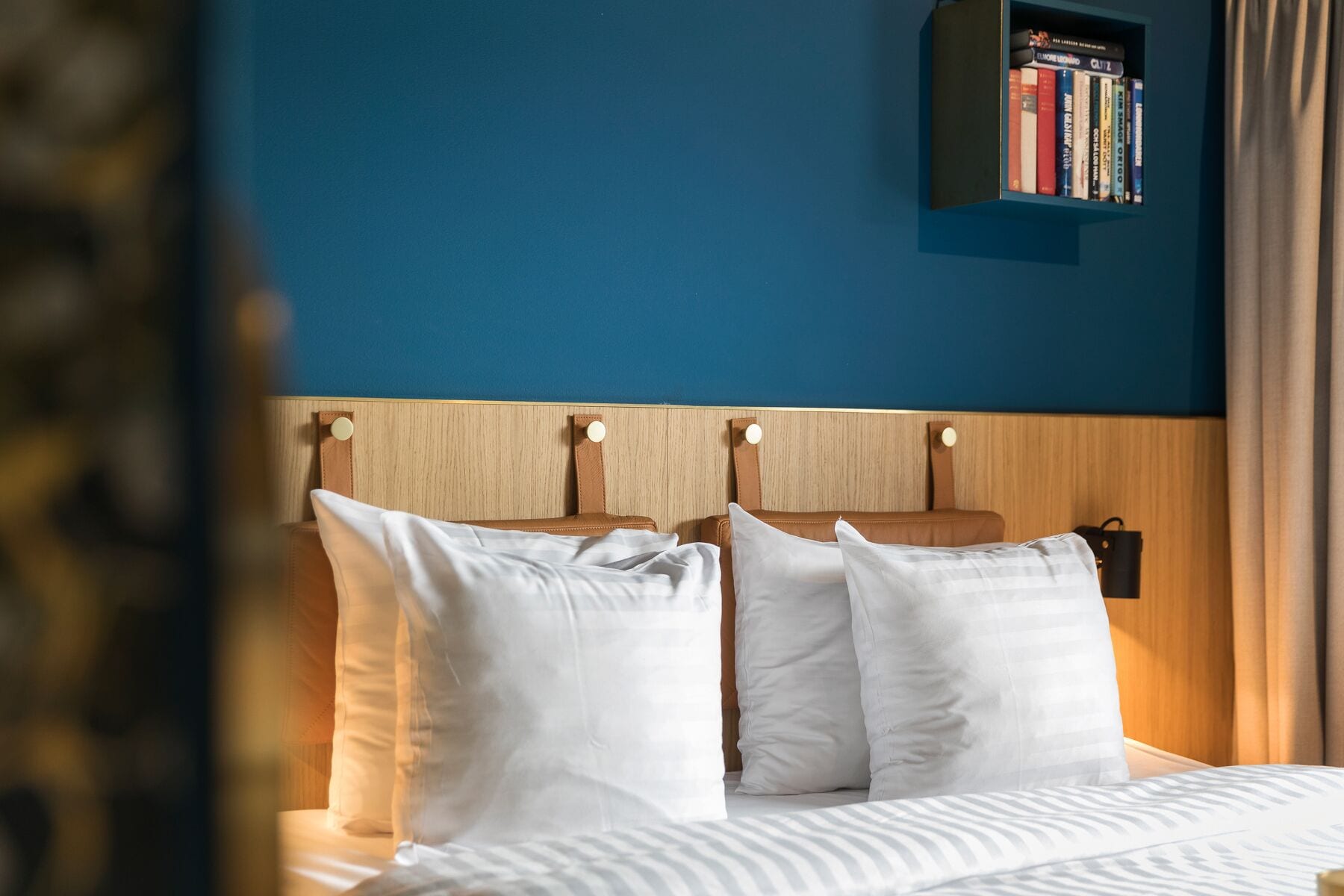 A neatly made bed with white linens and pillows, a wooden headboard with circular knobs, and a small bookshelf above it.