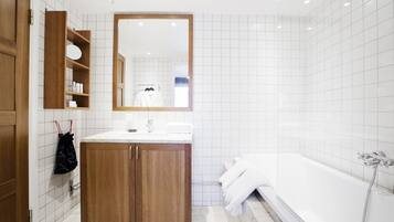 Un baño moderno con tocador de madera, un espejo grande, una bañera y paredes de azulejos blancos.
