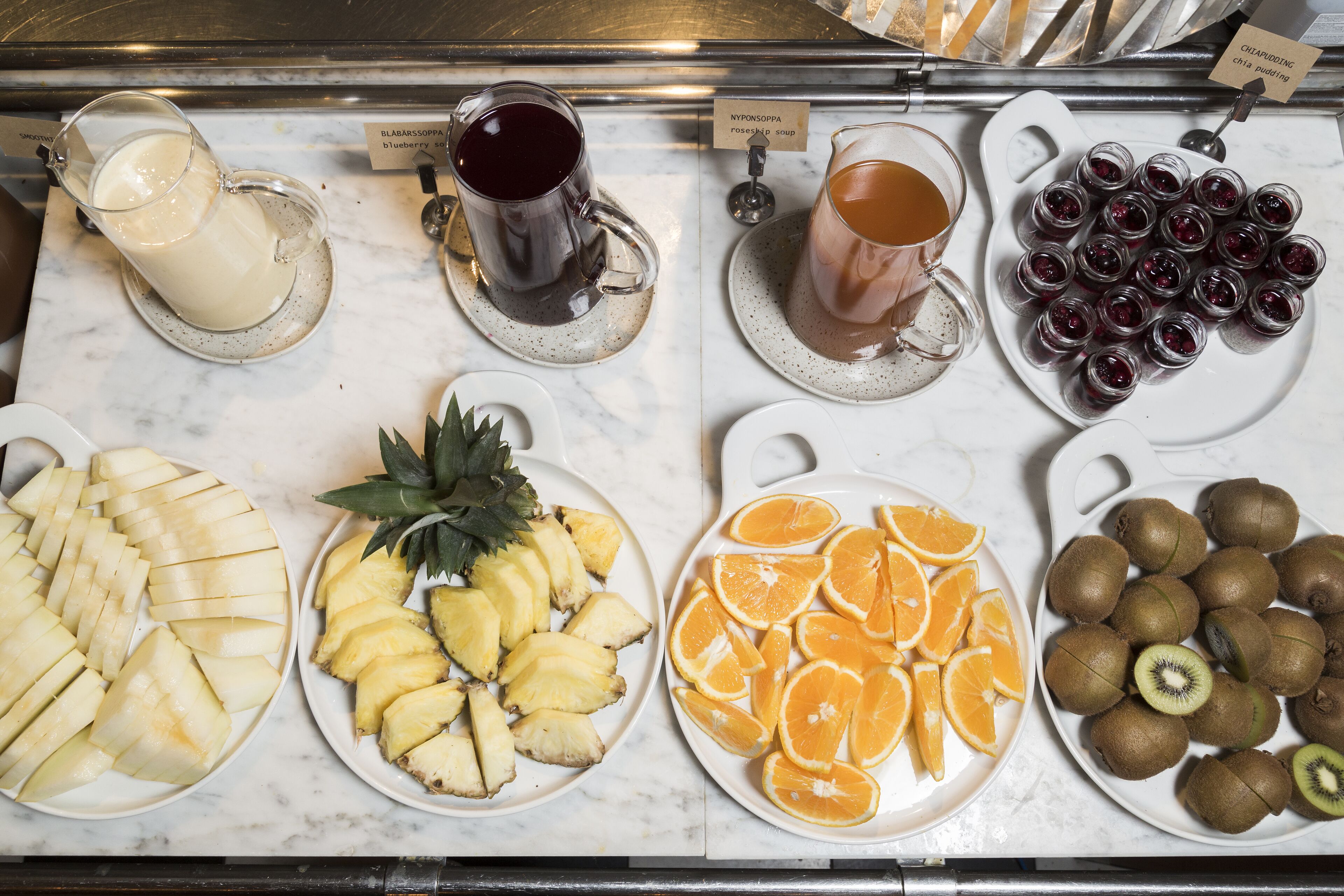 Se exhiben diversas frutas y bebidas, como piñas en rodajas, naranjas, kiwis, además de una variedad de jugos y siropes.