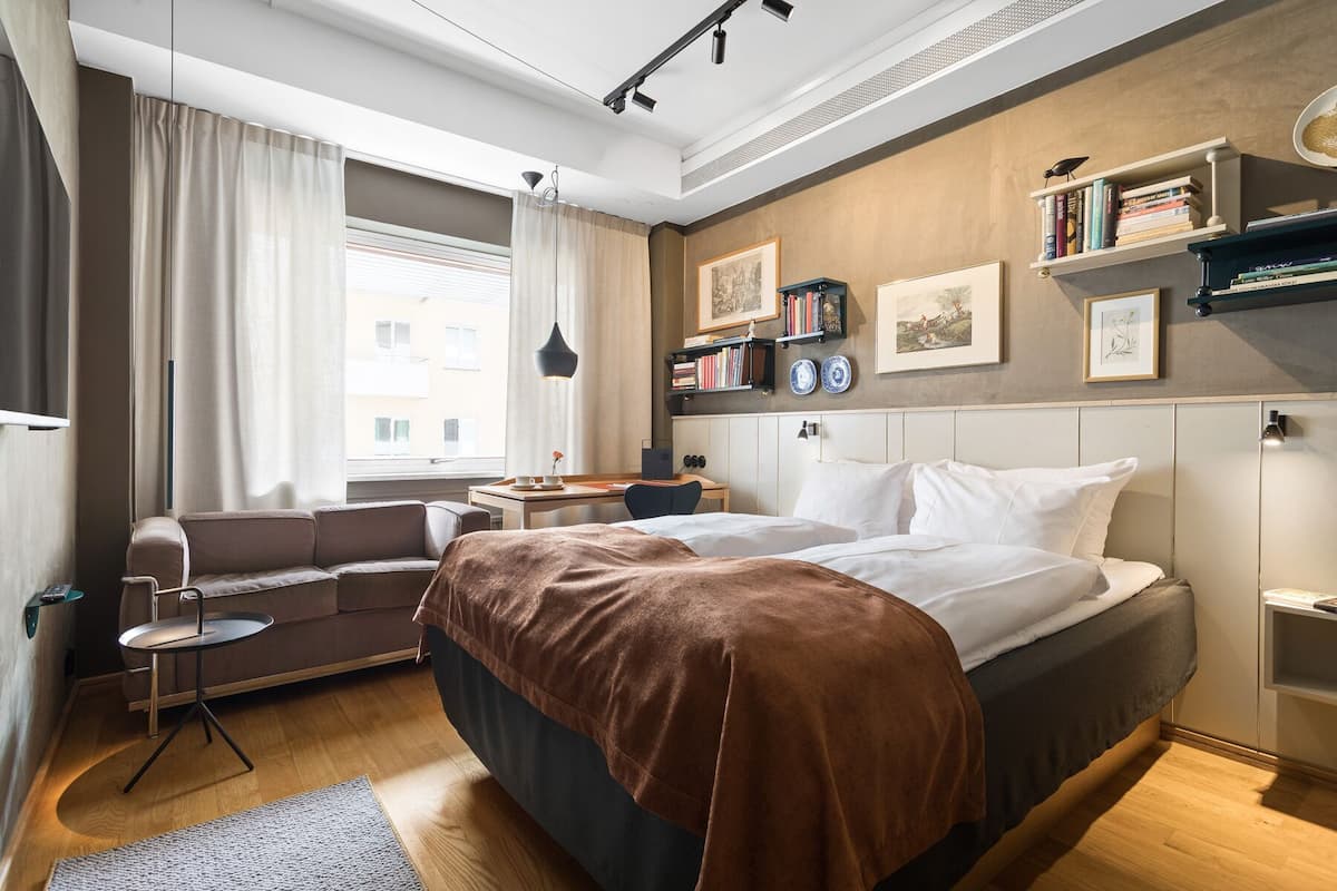 Una habitación de hotel moderna con una cama, un sofá, una mesita y una estantería.