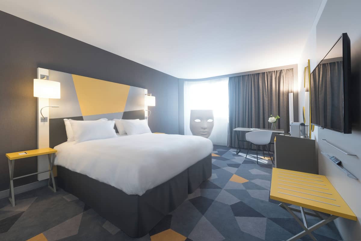 A hotel room with a large bed, a desk, a chair, and a TV.
