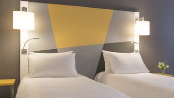 A hotel room with two beds, a modern headboard, bedside lamps, and a small vase with flowers.